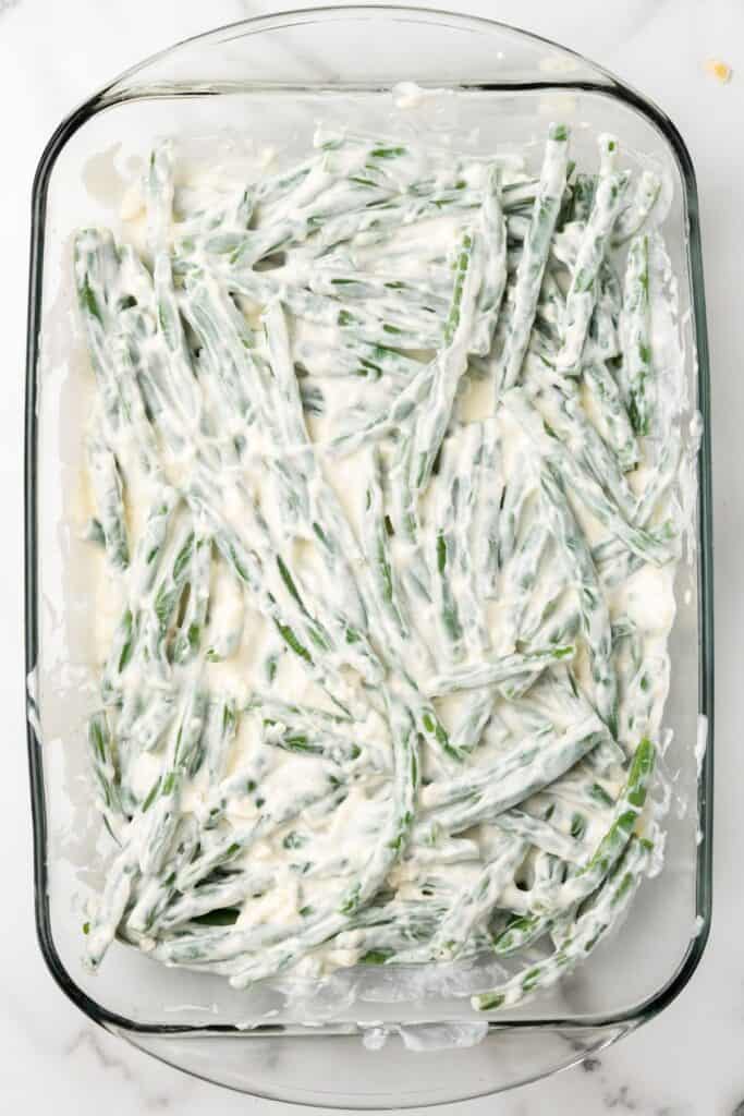 Green beans with a cream cheese mixture in a casserole dish.
