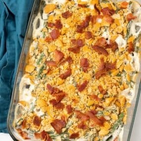 Finished green bean casserole in a casserole dish topped with bacon.