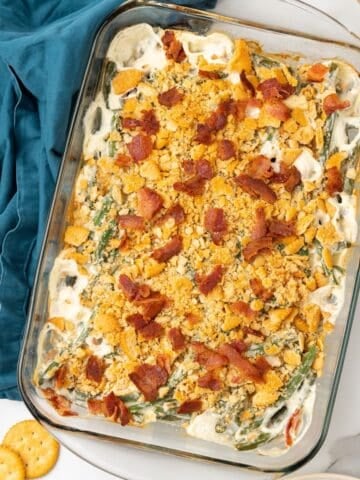 Finished green bean casserole in a casserole dish topped with bacon.