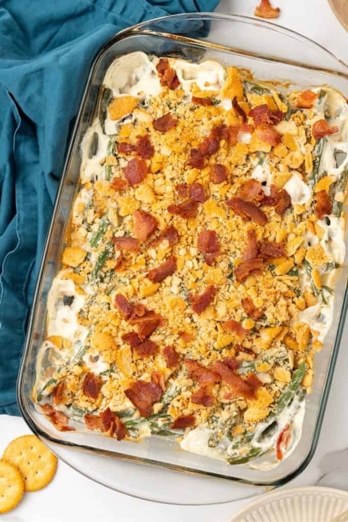 Finished green bean casserole in a casserole dish topped with bacon.