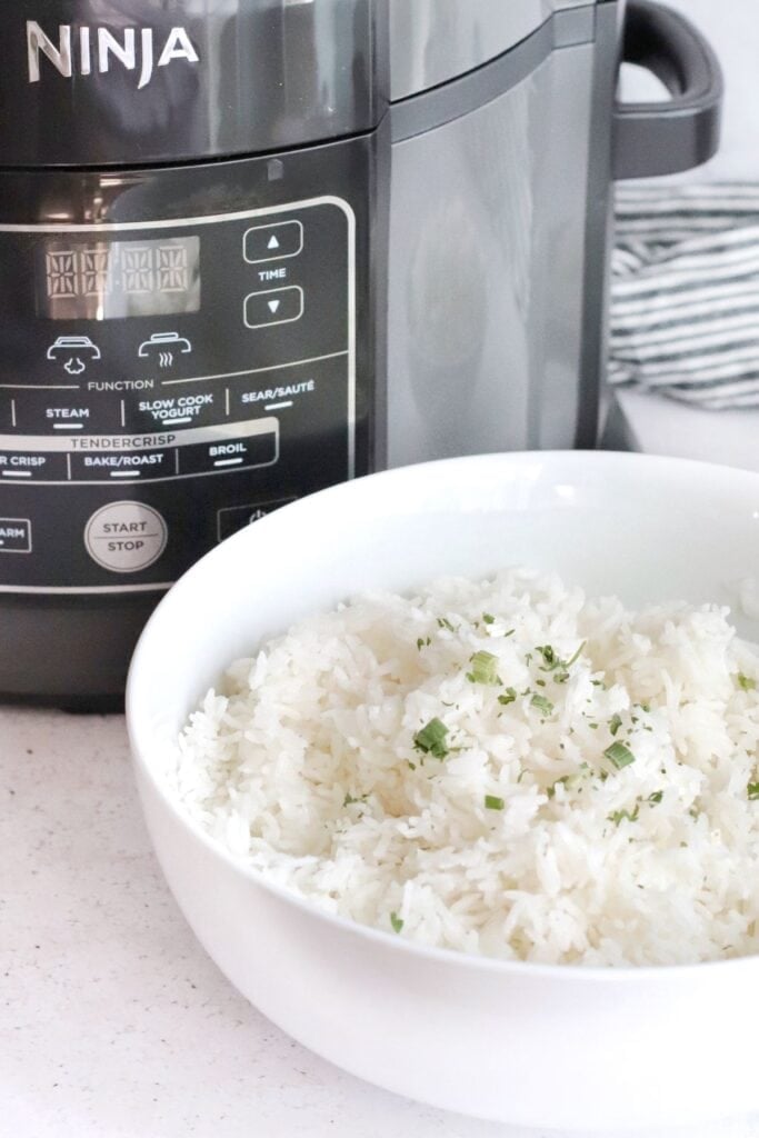 Cooked Ninja Foodi rice in a bowl in front of the Ninja Foodi pressure cooker/air fryer combo cooker.