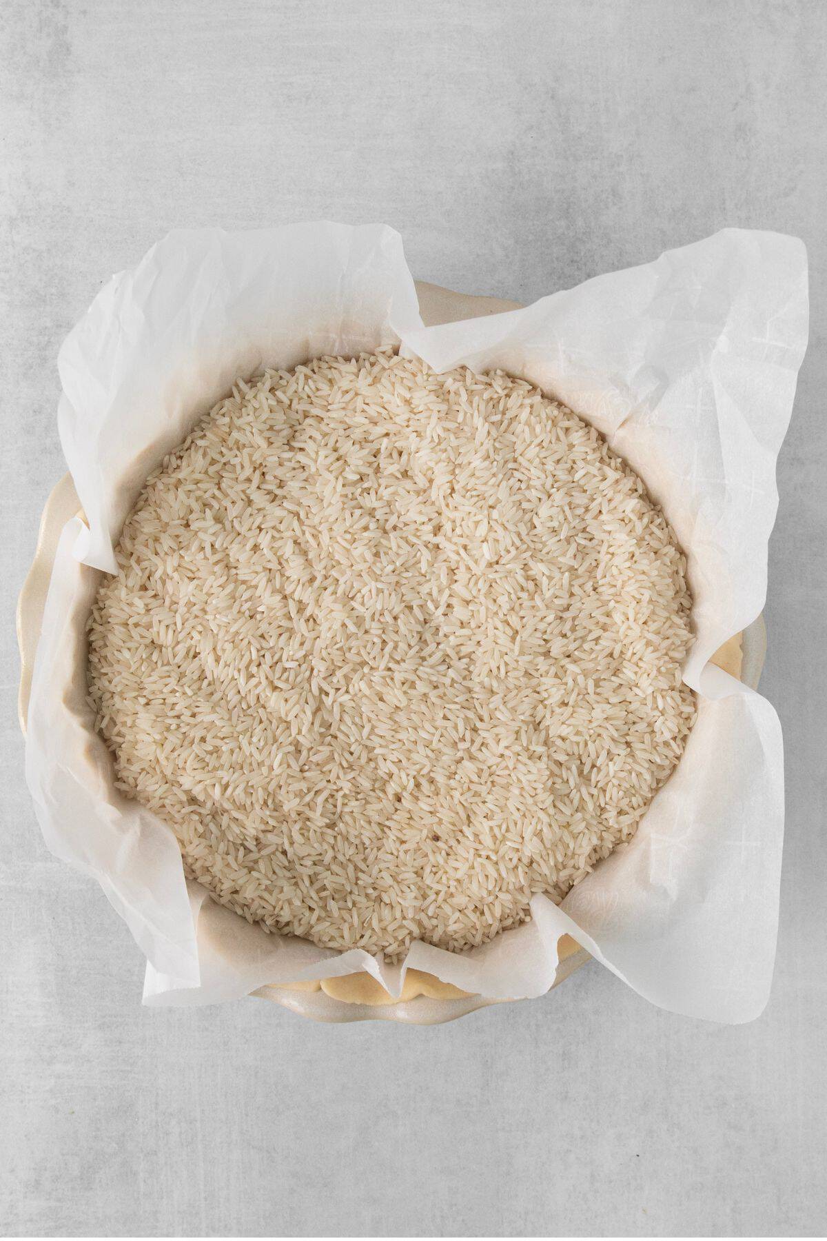 Pie pan with a pie crust covered with parchment paper and rice to keep the crust flat.
