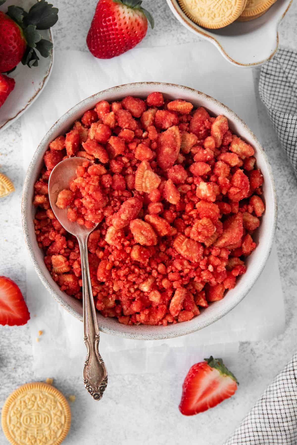 Strawberry crunch recipe in a bowl with a spoon in it surrounded by a couple fresh strawberries.