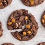Close up of the turtle cookie recipe with the middle one split in half so you can see the melted chocolate chips and caramel bits stretching.