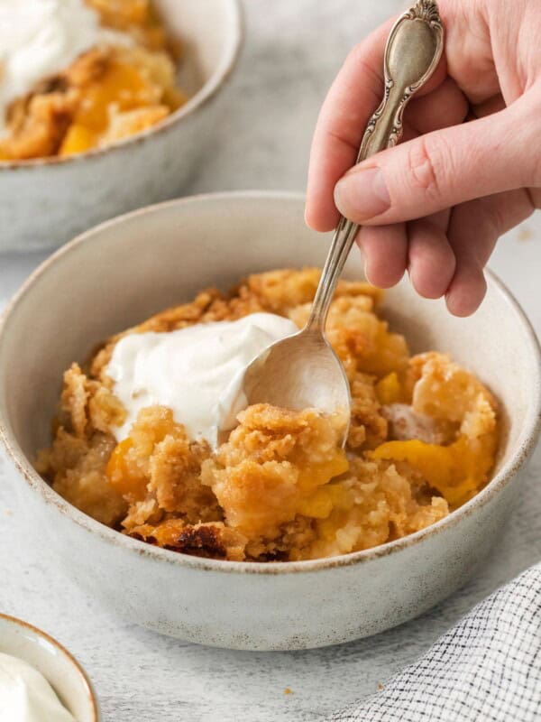 4 ingredient peach cobbler in a bowl with whipped cream with a spoon in it.