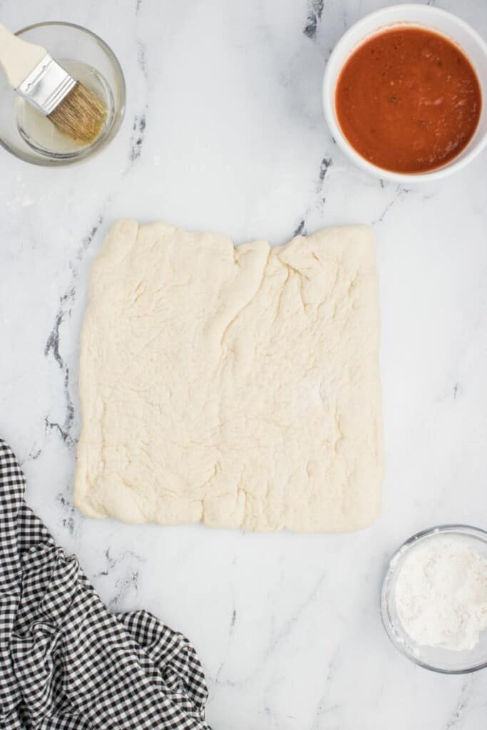 Rolling out pizza dough flat to prepare for toppings to be added.