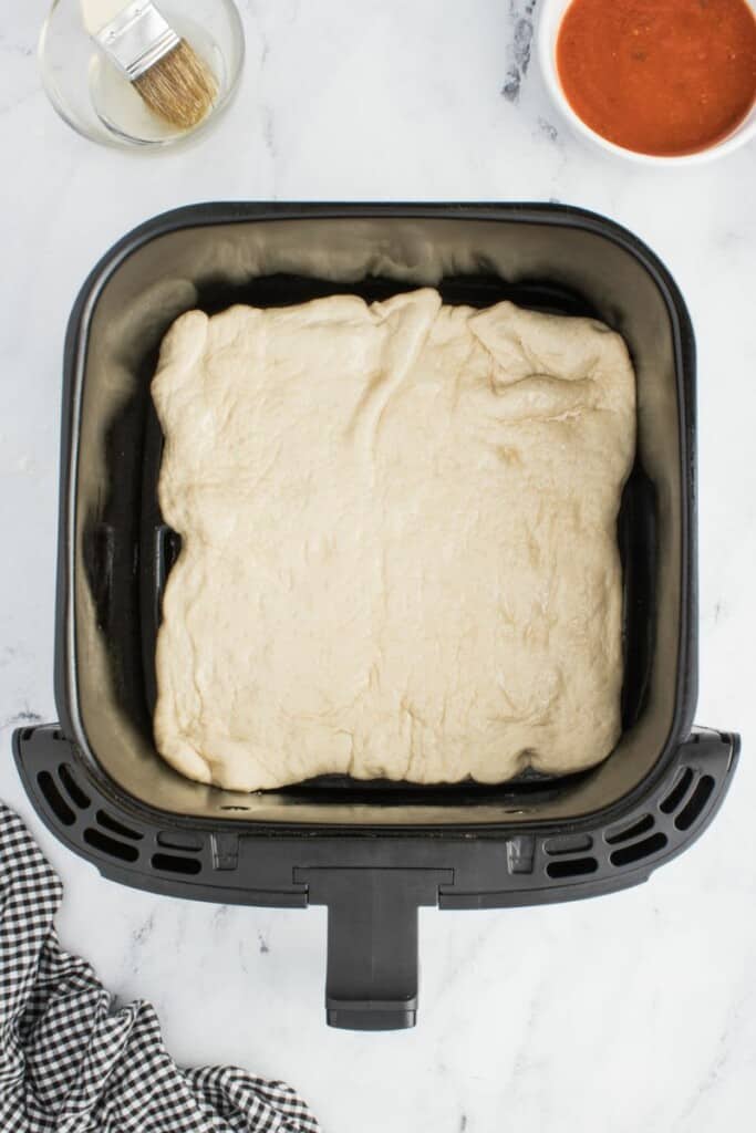 Flattened pizza dough in a black air fryer basket.