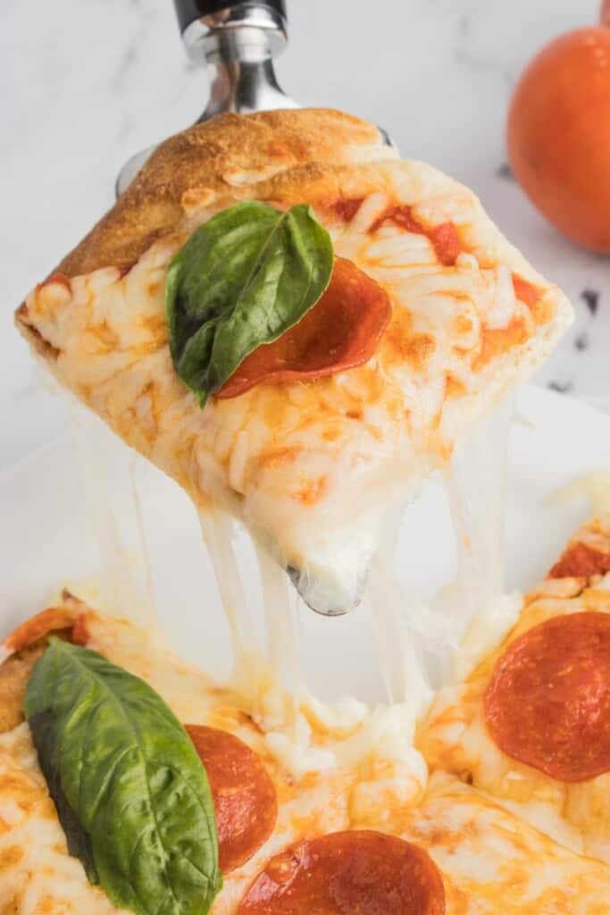 A serving fork holding a slice of pepperoni pizza with basil on top.