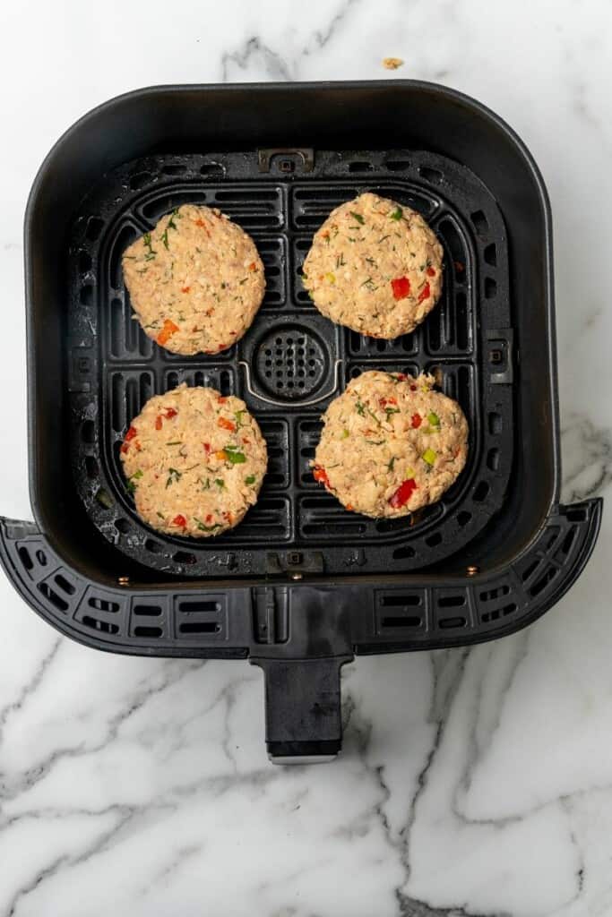 Four salmon patties resting in a black air fryer basket prepared to be cooked.