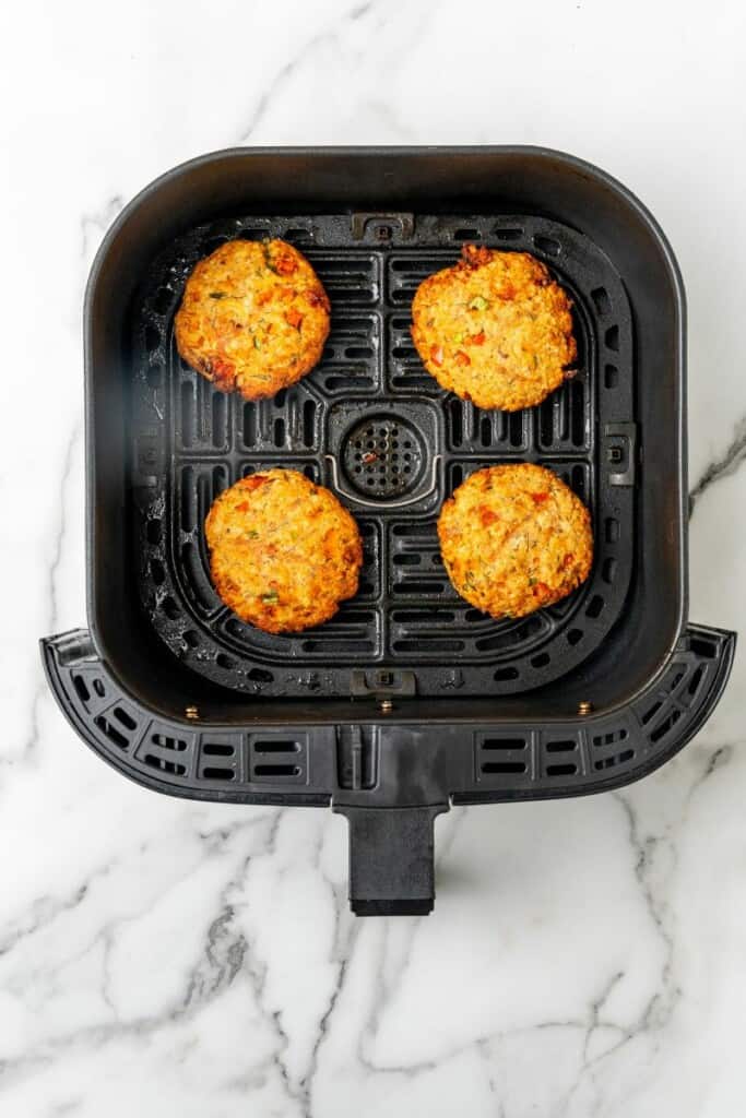 Four cooked salmon patties resting in a black air fryer basket.