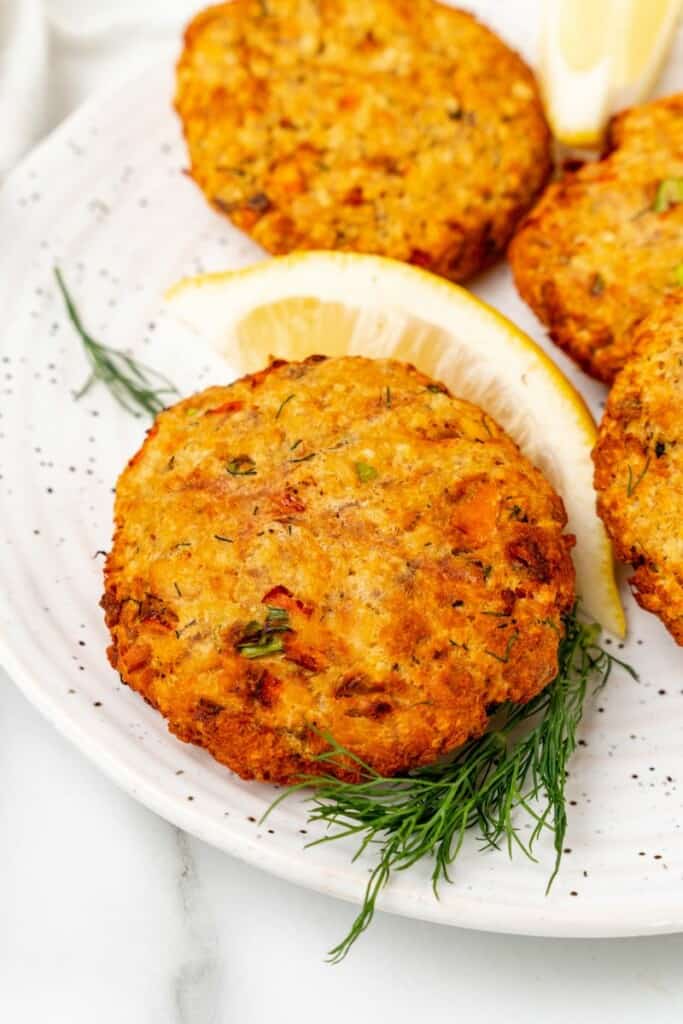 Closeup view of a prepared salmon patties on a speckled plate with lemon wedges.