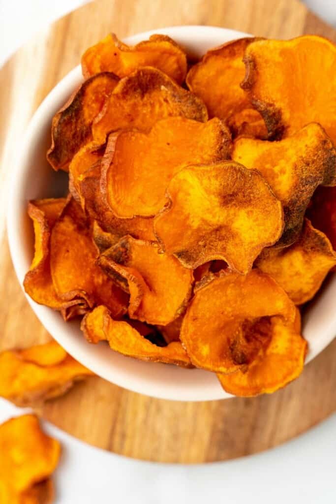 Sweet Potato Chips in a white bowl sitting on a wooden board.