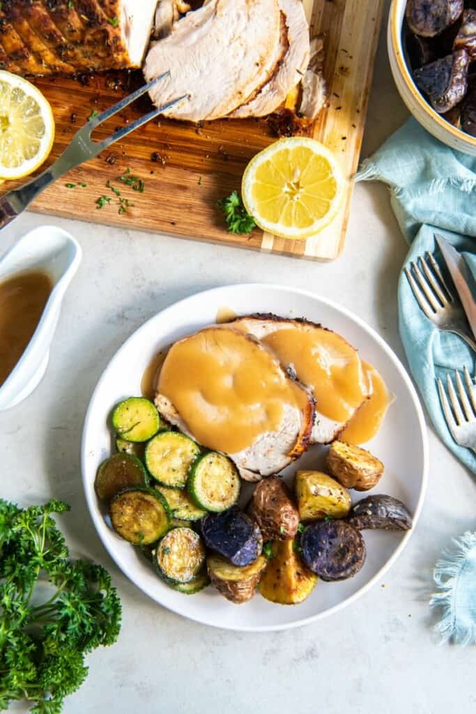 Sliced turkey breast on a white plate with vegetables.