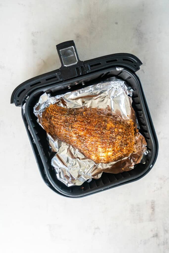 Seasoned turkey breast resting in a foil lined air fryer basket.