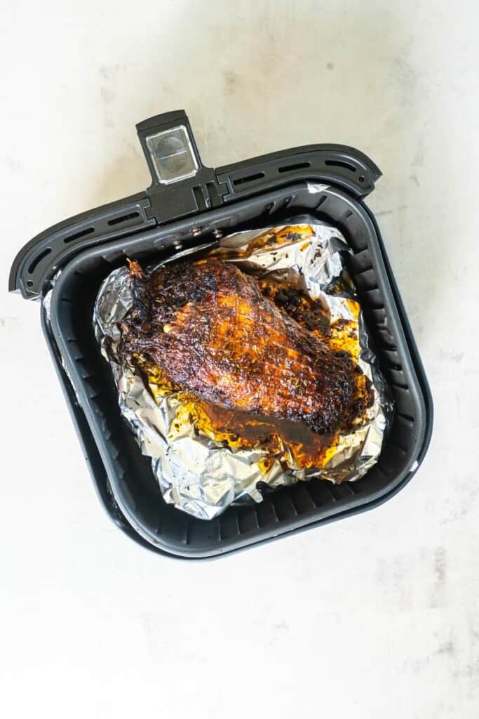 Fully cooked turkey breast resting in a foil lined air fryer basket.