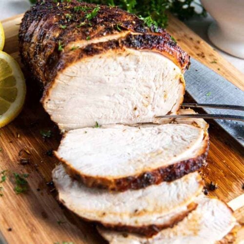 Turkey breast sliced and resting on a wooden cutting board.