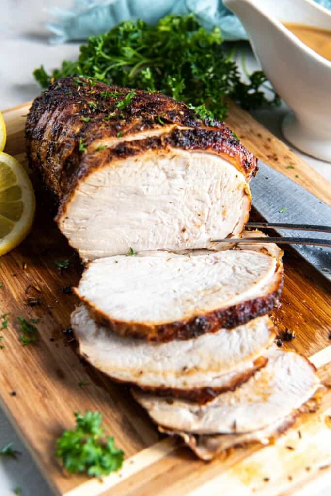 Turkey breast sliced and resting on a wooden cutting board.