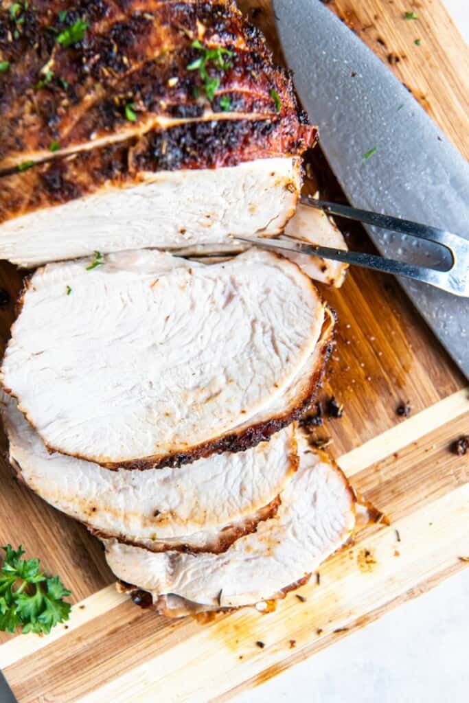 Close up view of sliced turkey breast on a wooden cutting board.