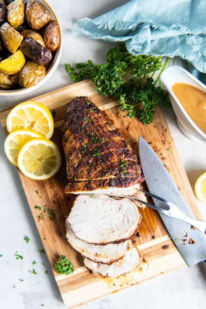 Overhead view of sliced turkey breast on a wooden cutting board with lemon slices.