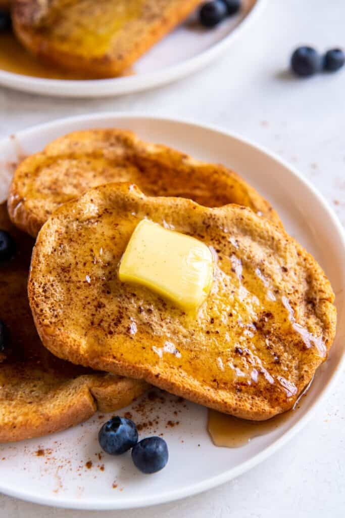 Air fried french toast with butter and maple syrup on it on a white plate.