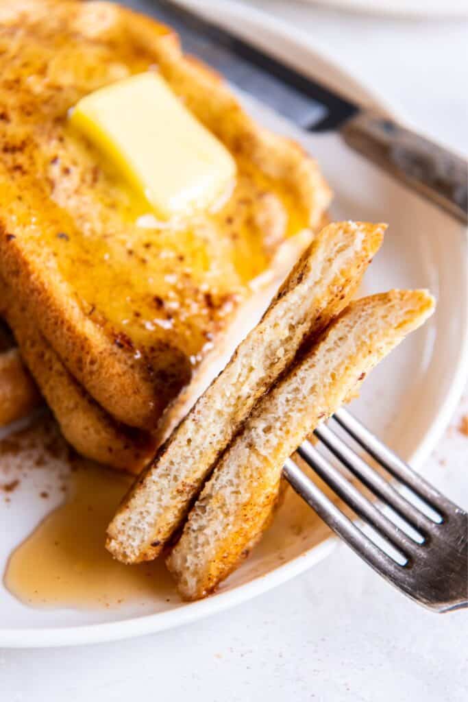 Slices of the air fry french toast on a fork with the rest of it next to it on a plate.