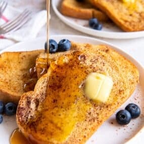 Air fryer french toast with butter on it, and maple syrup being poured on top of it.