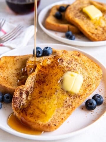 Air fryer french toast with butter on it, and maple syrup being poured on top of it.