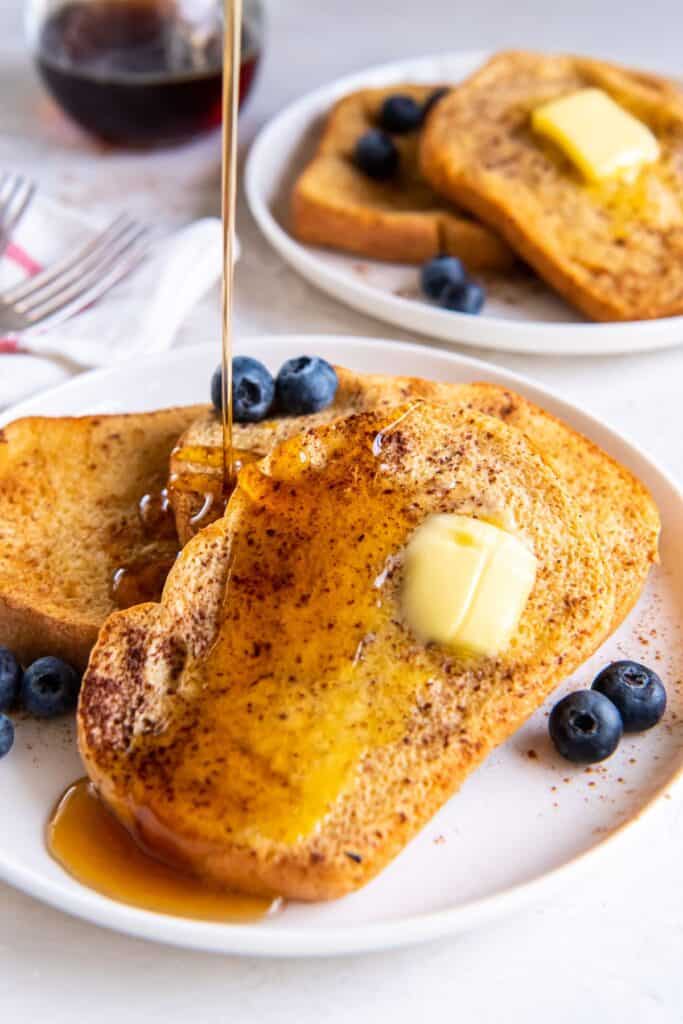 Air fryer french toast with butter on it, and maple syrup being poured on top of it.