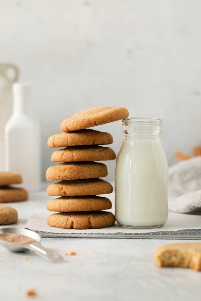 A stack of snickerdoodle cookies next to a small carafe of milk.