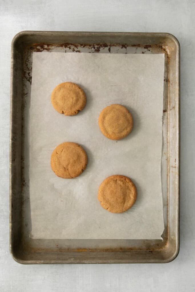 Baked snickerdoodles on a parchment lined cookie sheet.