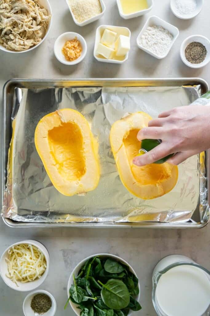 Spraying the inside of a scooped out spaghetti squash with cooking spray.
