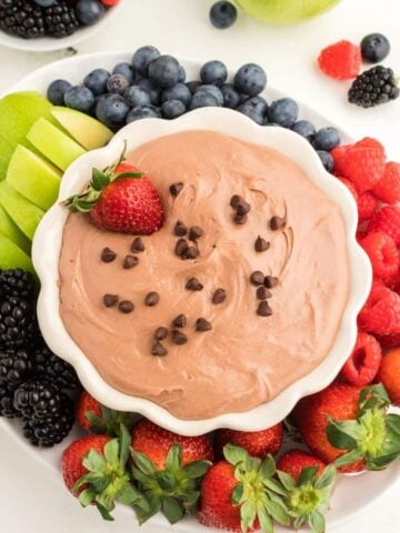 A white bowl of chocolate fruit dip topped with chocolate chips and a strawberry.