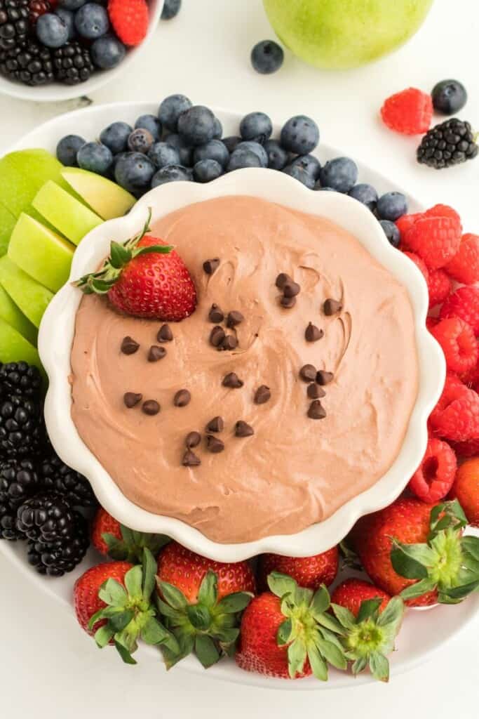 A white bowl of chocolate fruit dip topped with chocolate chips and a strawberry.