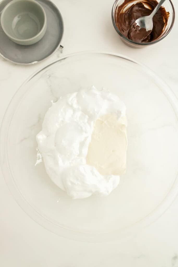 Combining cream cheese and cool whip in a clear mixing bowl.