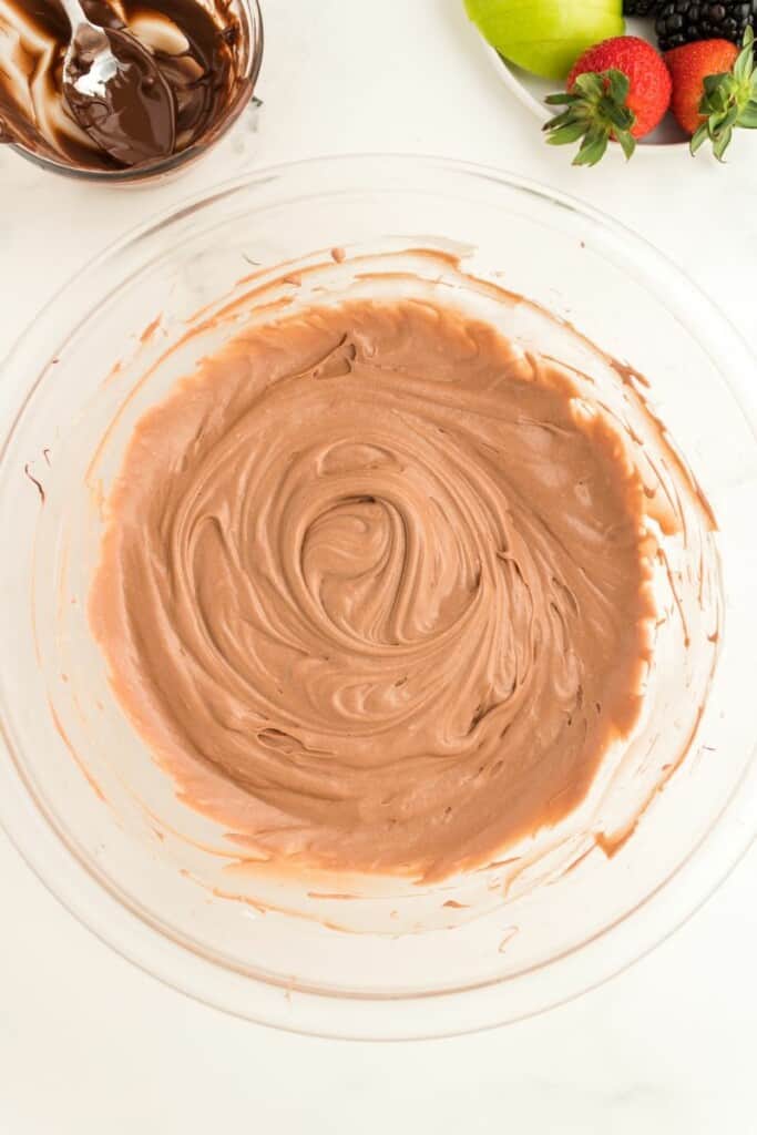 Melted chocolate chips combined with cream cheese mixture in a clear mixing bowl.