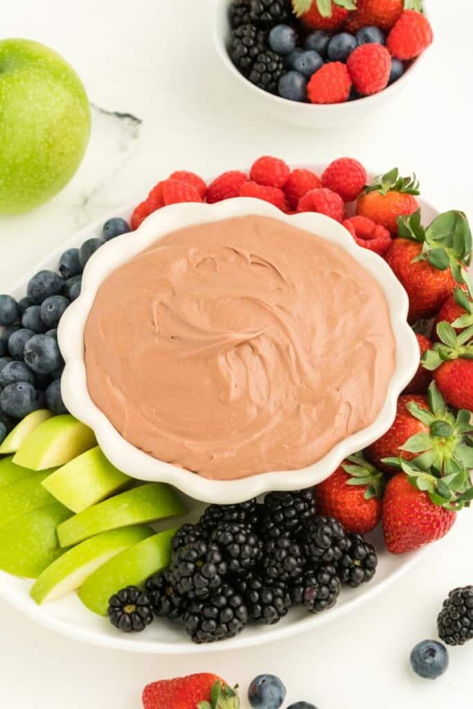 A bowl of chocolate fruit dip surrounded by fresh fruit.