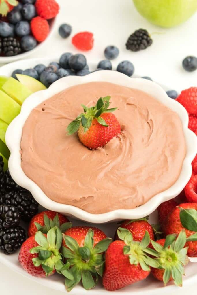 A white bowl of chocolate fruit dip topped with a strawberry dipped into it.