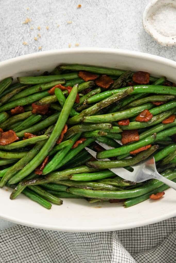Horizontal view of green beans and bacon in an oblong serving dish.