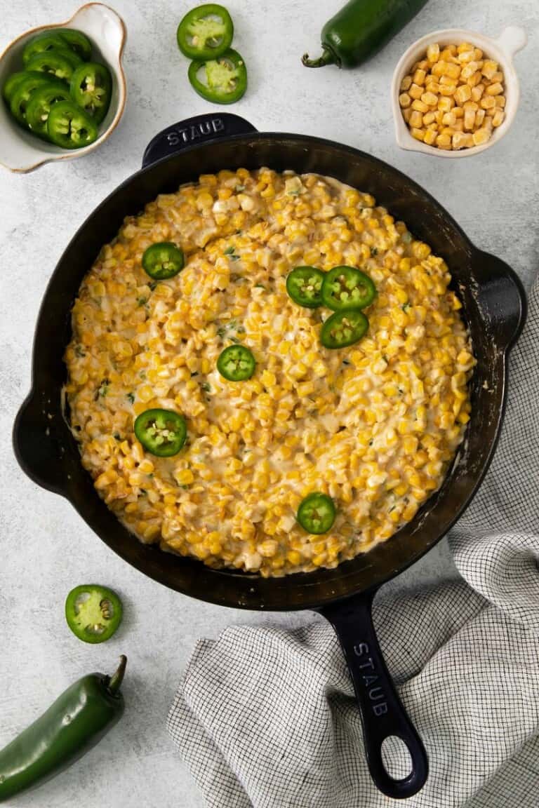 Creamed corn topped with slices of jalapenos in a cast iron skillet.