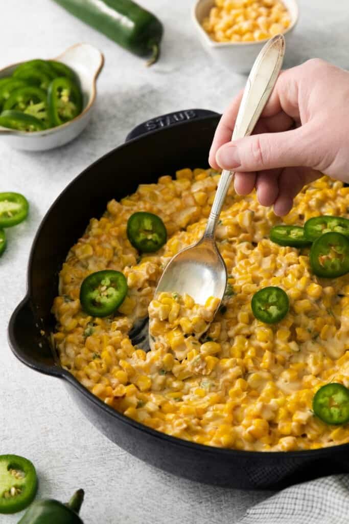 A spoon holding a bite of corn in a cast iron skillet of cream jalapeno corn.