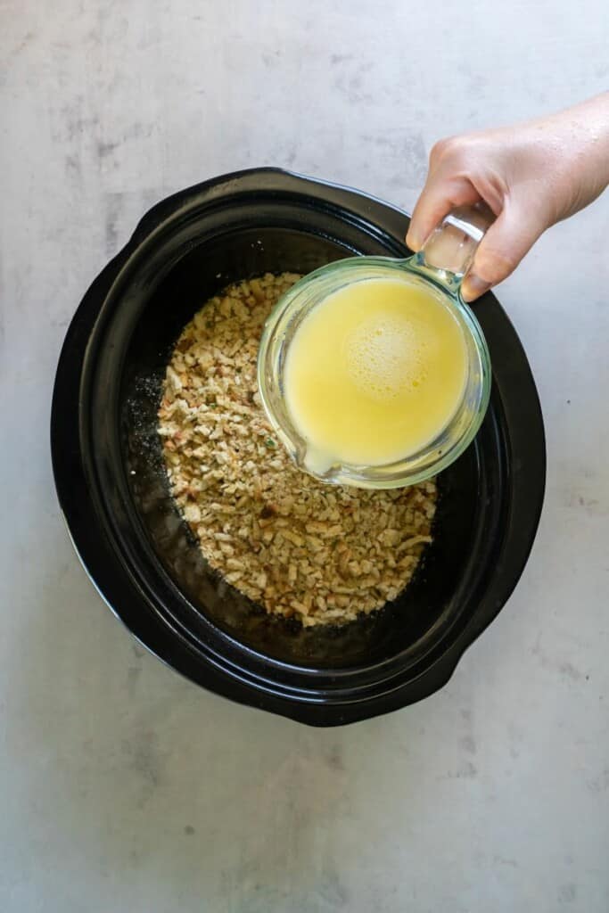 Pouring whisked melted butter over stuffing in a crock pot.