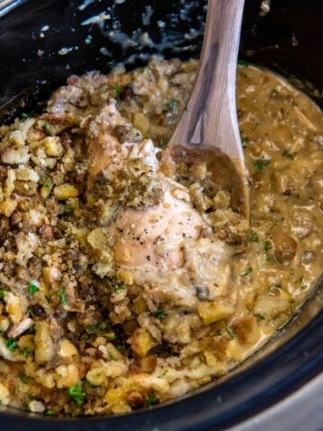 A wooden spoon lifting chicken and stuffing in a crock pot.