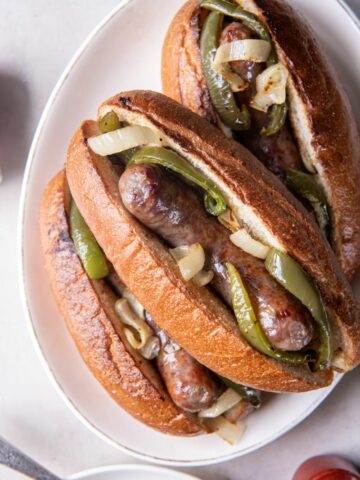 Three brats with toppings on a white plate.