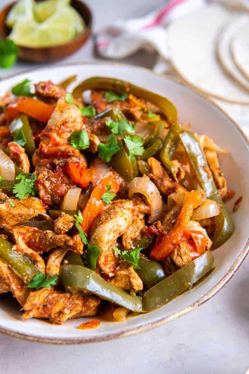 Close up view of seasoned chicken, onions and peppers for fajitas on a white plate.