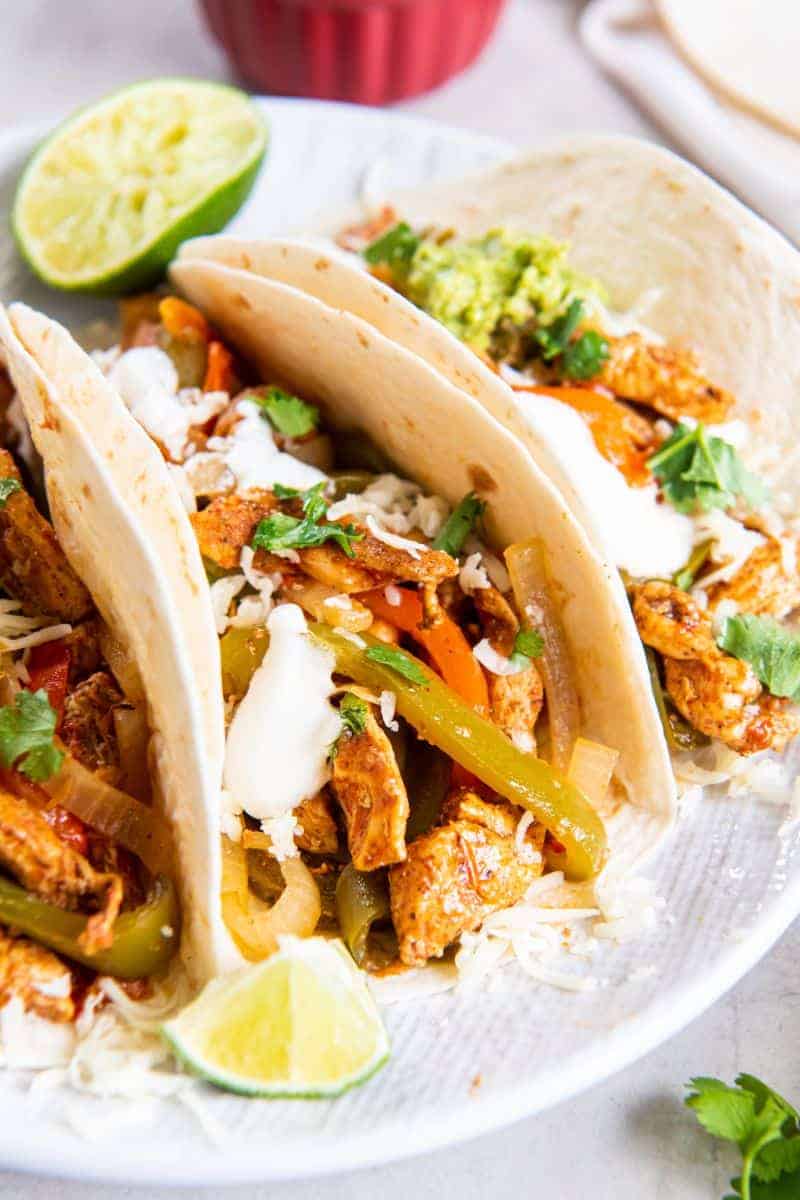 Three chicken fajitas with toppings resting on a white plate.