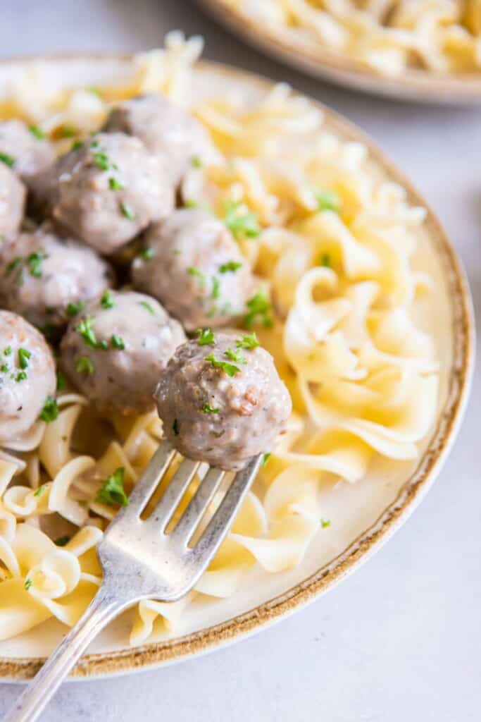 A fork holding a meatball above a bowl of pasta and meatballs.
