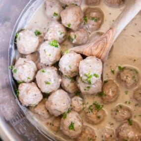 A wooden spoon lifting prepared meatballs in an Instant Pot.