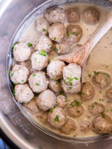 A wooden spoon lifting prepared meatballs in an Instant Pot.