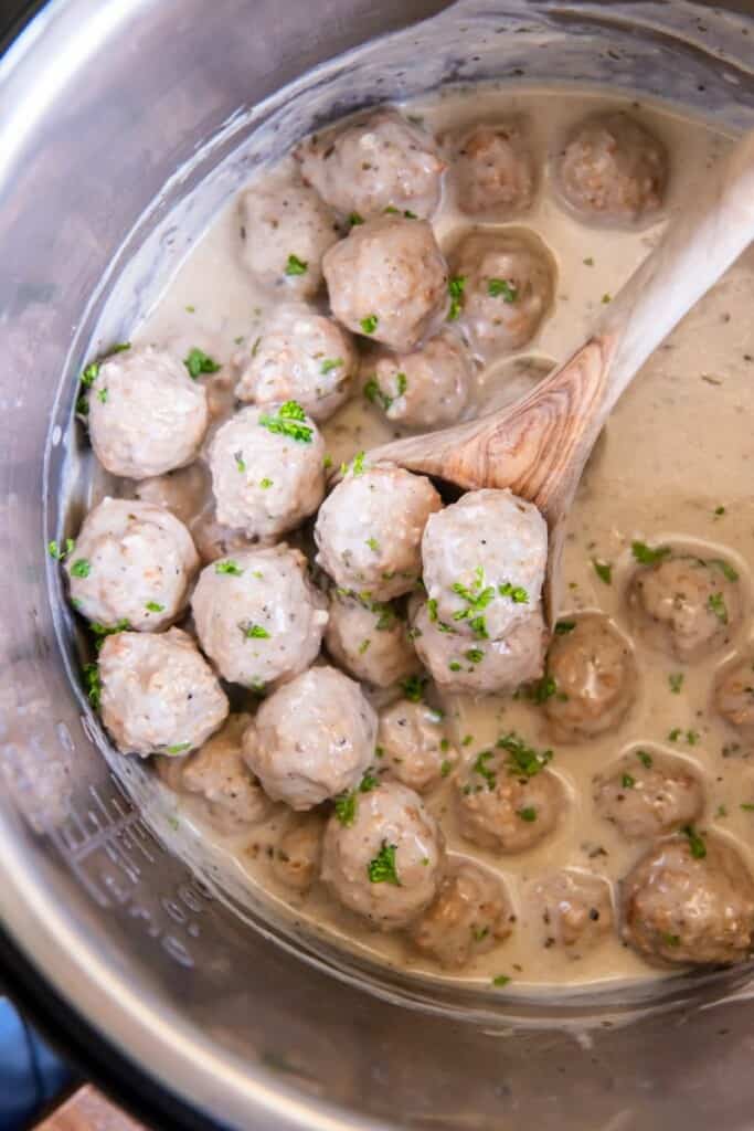 A wooden spoon lifting prepared meatballs in an Instant Pot.