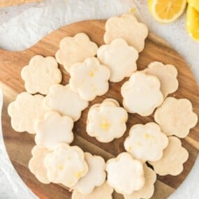 A batch of glazed lemon shortbread cookies on a wooden serving platter.